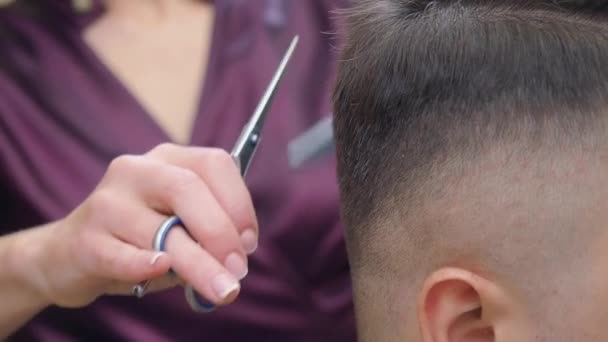 Close shot van stylisten handen knippen mans haar met schaar en kam. Vrouw in donkerrode jurk aan het werk in kapsalon. Selectieve zachte focus. Wazige achtergrond. — Stockvideo