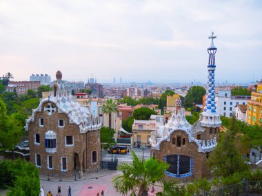 Barselona, İspanya - Ağustos 2019: Antonio Gaudi tarafından tasarlanan Park Guell 'in üst görüşü. Evler, kule ve parktaki turistler. Yoğun bulutlu gökyüzü. Seçici yumuşak odaklanma. Bulanık arkaplan.