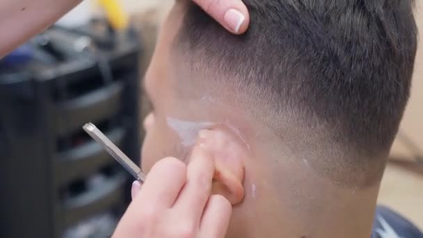 Barber scheert klanten tempel met open scheermes, dichtbij schot. Stylist aan het werk in kapsalon. Man in de kapperszaak. Selectieve zachte focus. Wazige achtergrond. — Stockvideo
