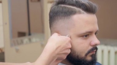 Kuaförde kuaför, yakın çekim. Usta kesme makinesiyle erkek saçı kesiyor. Berber dükkanındaki adam. Seçici yumuşak odaklanma. Bulanık arkaplan.