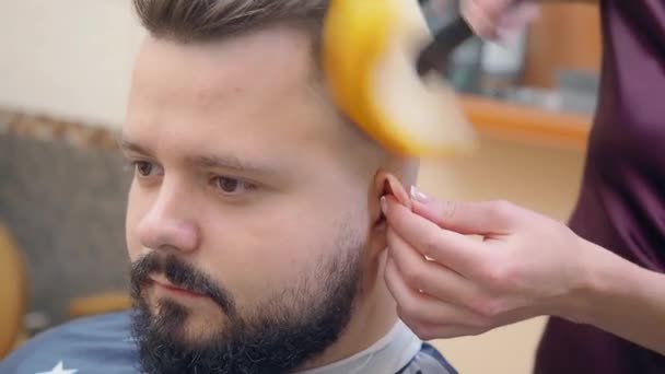 留着胡子的男人在理发店里，近距离射击。 发型师用剪短的头发清洁客户的脸。 理发店里的人 有选择的软焦点。 模糊的背景. — 图库视频影像