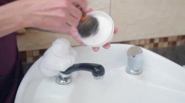 Stilist fırçayla tıraş köpüğü hazırlıyor, yakın çekim. Burbershop 'un içi. Berber, beyaz lavabonun yanında duruyor. Seçici yumuşak odaklanma. Bulanık arkaplan.