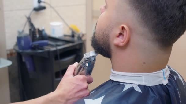 Man in kapperszaak, baard knipproces, close shot. Styliste snijdt mannetjes baard met tondeuse. Opgenomen in kapsalon. Selectieve zachte focus. Wazige achtergrond. — Stockvideo