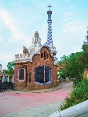 Barselona, İspanya - Ağustos 2019: Kulesi, kaldırımı ve yeşil bitkileri olan renkli bir ev, orta ölçekli bir manzara. Barcelona 'daki Park Guell, Antonio Gaudi tarafından tasarlandı. Seçici yumuşak odaklanma. Bulanık arkaplan.