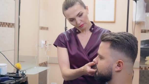 Jovem mulher corte de cabelo clientes com clipper, tiro de perto. Homem no salão de cabeleireiro. Interior da barbearia. Foco suave seletivo. Fundo desfocado . — Vídeo de Stock