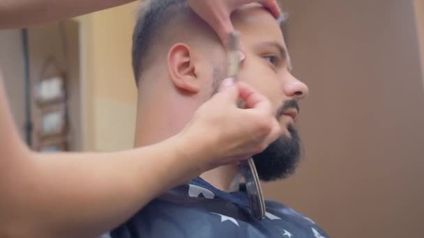 Estilista en vestido rojo oscuro afeitar clientes cuello con navaja abierta, tiro cerrado. Hombre en la peluquería. Interior del salón de peluquería. Enfoque suave selectivo. Fondo borroso . — Vídeo de stock