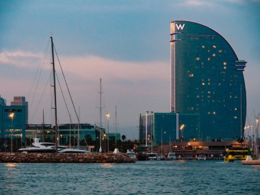 Barselona, İspanya - Ağustos 2019: Rıhtımda bir sürü yat, uzun görüş... deniz kıyısındaki modern yüksek bina. Mavi bulutlu gökyüzü. Deniz yüzeyi dalgalanması. Seçici yumuşak odaklanma. Bulanık arkaplan.