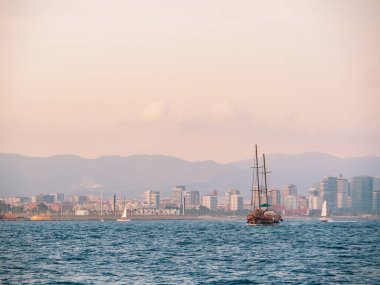 Barselona, İspanya - Ağustos 2019: Akdeniz 'de birkaç yat, ekstra uzun manzara. Deniz kenarındaki modern binalar. Ufuktaki yüksek tepeler. Sisli bir gökyüzü. Seçici yumuşak odaklanma. Bulanık arkaplan.