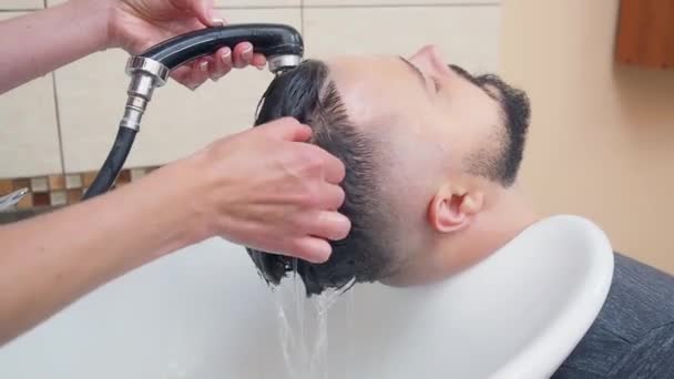 Lavar a cabeça após o corte de cabelo, tiro de perto. Cabelo de clientes de lavagem estilista, gravado na barbearia. Interior do salão de cabeleireiro. Foco suave seletivo. Fundo desfocado . — Vídeo de Stock