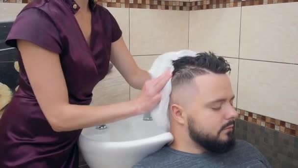 Feminino em vestido vermelho escuro limpando o cabelo dos homens com toalha branca, tiro de perto. Homem no salão de cabeleireiro. Interior da barbearia. Foco suave seletivo. Fundo desfocado . — Vídeo de Stock