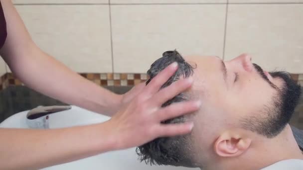 Στυλίστρια πλύνετε το κεφάλι των πελατών με σαμπουάν σε λευκό washstand, κοντά shot. Άντρας στο κομμωτήριο. Επιλεκτική μαλακή εστίαση. Θολή φόντο. — Αρχείο Βίντεο