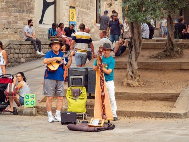 Barselona, İspanya - Ağustos 2019: Meydanda oynayan sokak müzisyenleri, Sagrada Familia Katedrali, orta manzara. Turistler oturup müzik dinlerler. Seçici yumuşak odaklanma. Bulanık arkaplan.