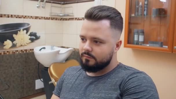 Homme après la coupe de cheveux dans le salon de coiffure, plan rapproché. Le client regarde sa nouvelle coiffure dans un miroir. Intérieur du salon de coiffure. Mise au point sélective. Fond flou . — Video