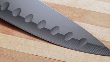 Black knifes blade, close shot. Dolly shot knife blade from point to handle. Background of kitchen knife laying on table. Texture of wooden table.