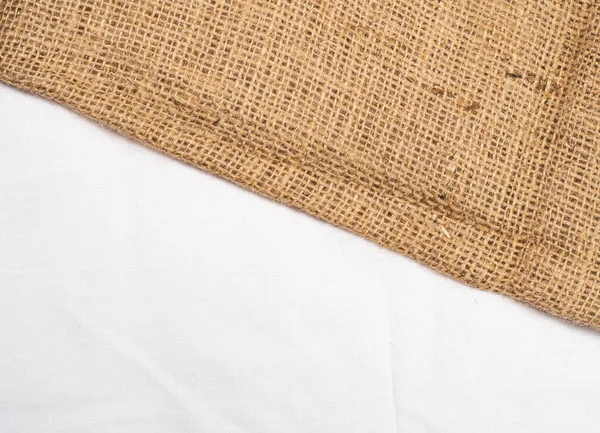 Brown burlap laying on white sheet, close up view. Abstract background. Texture of sackcloth. Background for banners, or wallpapers.