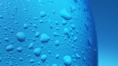 Plastik şişe suyunun yüzeyindeki buğulanma, yakın çekim. Şişeden süzülen su damlası, kapat. Soyut mavi arkaplan. Seçici yumuşak odaklanma. Bulanık arkaplan.