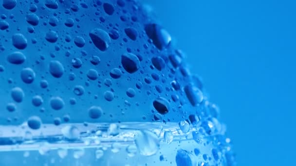 Makroaufnahme von Wassertropfen auf Flaschenoberfläche. Schuss einer Plastikflasche, die mit Kondensat bedeckt ist. Abstrakter blauer Hintergrund. Selektiver weicher Fokus. Unklarer Hintergrund. — Stockvideo