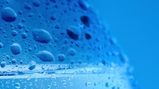 Er valt veel water op het flesoppervlak, macro shot. Dolly shot fles bedekt met condensaat. Abstracte blauwe achtergrond. Selectieve zachte focus. Wazige achtergrond. — Stockvideo