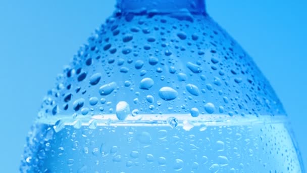 Close shot of water drops on bottle surface. Dolly shot of bottle of table water covered with condensate. Abstract blue background. Selective soft focus. Blurred background. — Stock Video