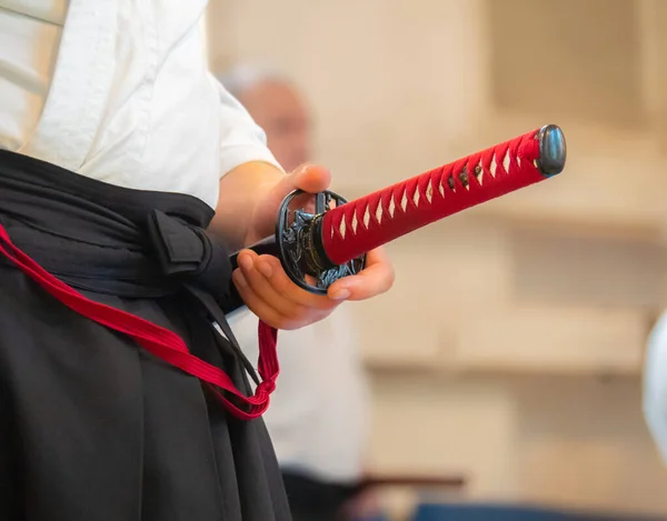 El hombre vestido con keikogi y hakama se queda con la espada japonesa de cerca. Instructor de artes marciales con Katana en el seminario. Vista frontal —  Fotos de Stock
