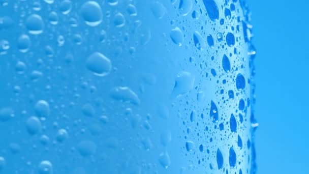 A lot of water drops on bottle surface, macro shot. Camera slowly sliding along bottle of table water covered with condensate. Abstract blue background. Selective soft focus. Blurred background. — Stock Video