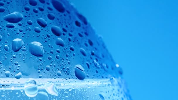 L'eau tombe sur une bouteille d'eau de table, macro shot. Dolly shot de bouteille recouverte de condensat. Fond bleu abstrait. Mise au point sélective. Fond flou . — Video