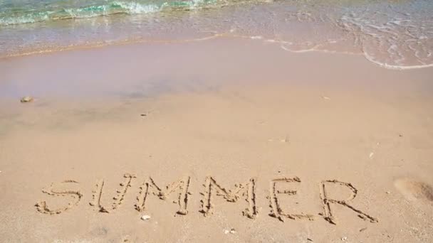 Napis na żółtym piasku, średni strzał z bliska. Woda morska płynąca po plaży. Fotografia w Hurghadzie, Morze Czerwone w lutym. Selektywne miękkie skupienie. Zamazane tło. — Wideo stockowe