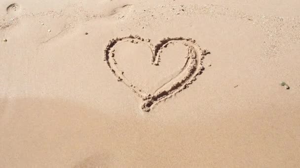 Hjärtat målat på gul sand med finger, närbild. Röda havets vågor raderar hjärtat målat på sand. Fotograferad på egyptisk strand i februari. Selektivt mjukt fokus. suddig bakgrund. — Stockvideo