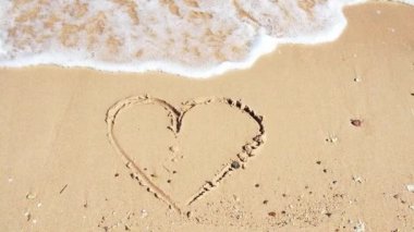 Kalbi sarı kuma boyanmış, yakın çekim. Kızıl Deniz dalgaları, sarı kuma parmak çizerek kalbi siliyor. Şubat ayında Hurghada plajı. Seçici yumuşak odaklanma. Bulanık arkaplan.