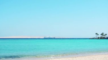 Kızıl Deniz 'de yelken açan beyaz turistik gemi, çok geniş açılı. Açık mavi gökyüzünün altında yeşil palmiye ağaçları. Şubatta Hurghada 'da çekilmiş. Seçici yumuşak odaklanma. Bulanık arkaplan.