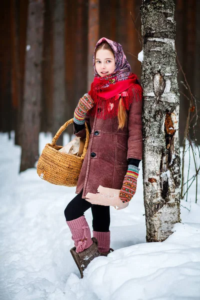 一个带着篮子的女孩在冬天的森林里站在一棵树旁 — 图库照片