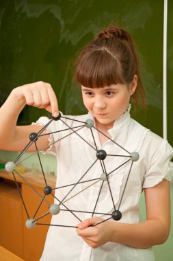 The school girl near the chalkboard holds in hands the model of molecules clipart