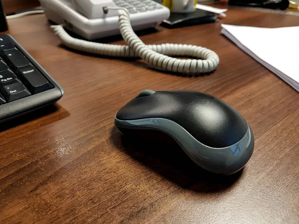 The small black wireless mouse on a wooden office desktop