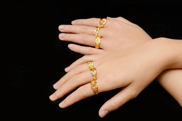 Рука женщины с различными золотыми кольцами на черном фоне — стоковое фото