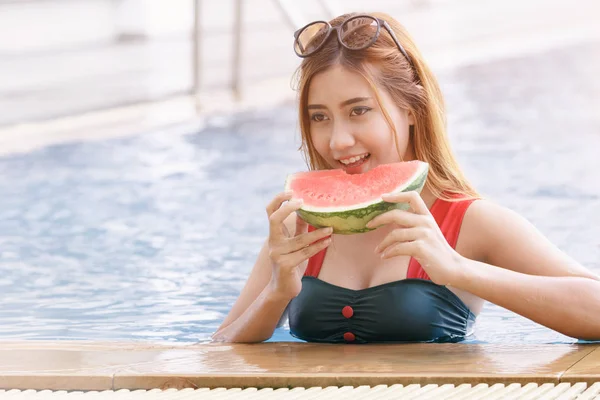 Asian woman eating watermelon in swimming pool