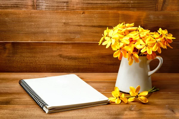 Yellow gardenia flower in vase with note book on wooden backgrou