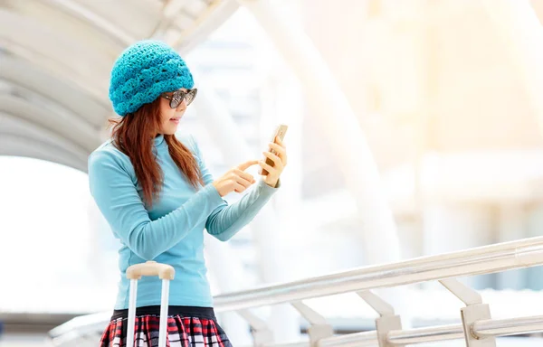 Mobilní telefon používat turistické dívka s kufrem na vlakovém nádraží — Stock fotografie