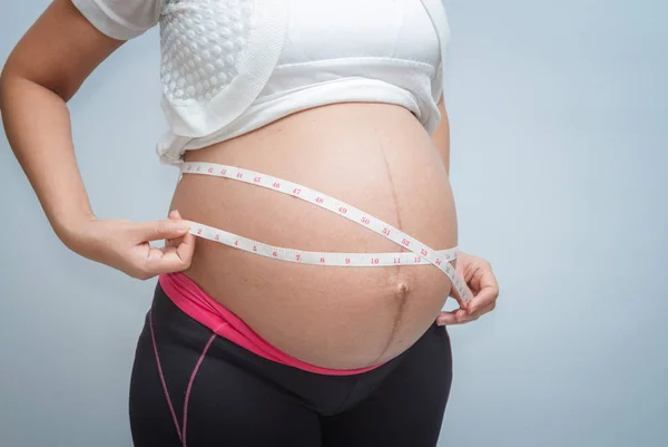 Nahaufnahme einer schwangeren Frau, die ihren Bauch auf weißem Hintergrund misst — Stockfoto