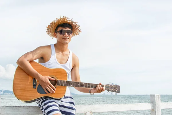 Młody mężczyzna gra na gitarze akustycznej na plaży — Zdjęcie stockowe