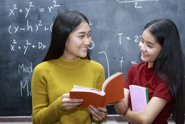 Two happy Asian college student reading books in the library tog