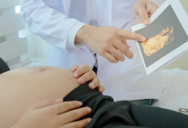 Femme enceinte est couchée au lit tandis que le médecin montrant l'ultrasou — Photo