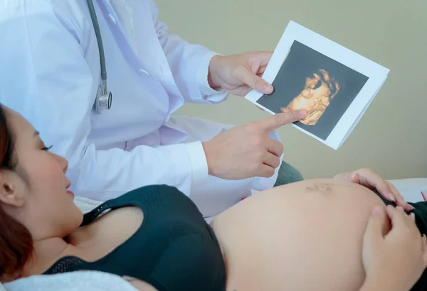 Femme enceinte est couchée au lit tandis que le médecin montrant l'ultrasou — Photo