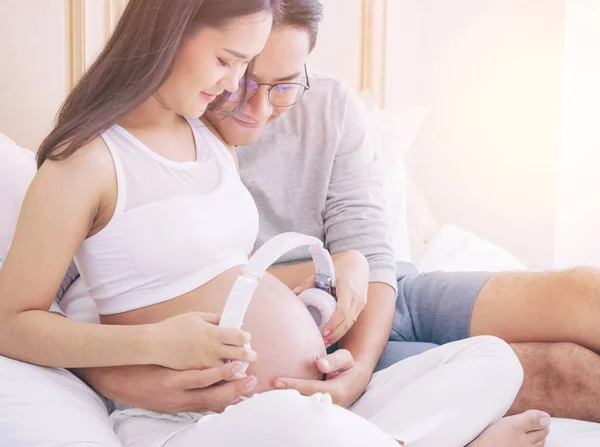 Femme enceinte et mari tenant des écouteurs sur le ventre jouer m — Photo