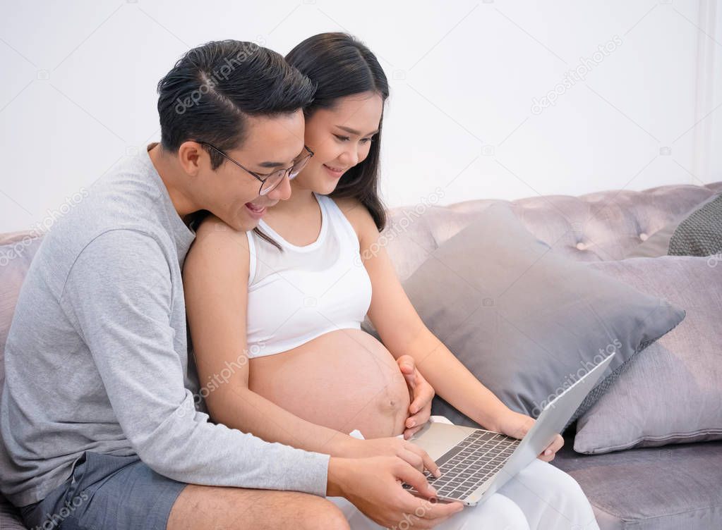 Pregnant woman and her husband useing laptop at home together