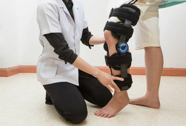 Fisioterapia femenina ajustando el corsé para caminar en la pierna de la paciente — Foto de Stock