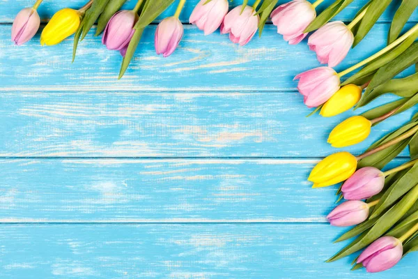 Bando de tulipas amarelas e rosa em um fundo de madeira azul . — Fotografia de Stock