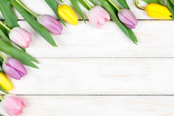 Um bando de tulipas cor-de-rosa e amarelas deitadas num backgrou de madeira branco — Fotografia de Stock