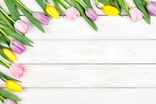 Um bando de tulipas cor-de-rosa e amarelas deitadas num backgrou de madeira branco — Fotografia de Stock