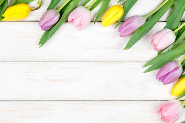 Um bando de tulipas cor-de-rosa e amarelas deitadas num backgrou de madeira branco — Fotografia de Stock