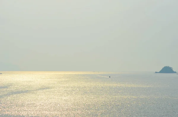 Küçük bir tekne, küçük bir adanın yakınında, parlak bir okyanusun üzerinde seyahat ediyor.. — Stok fotoğraf